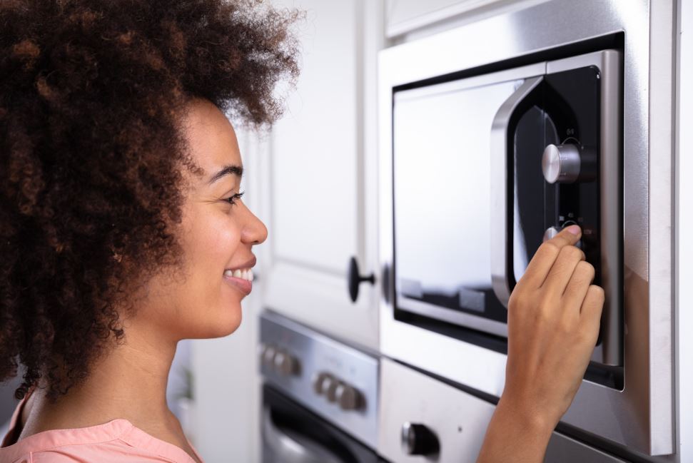 a smiling girl setting up the function of a microwave oven